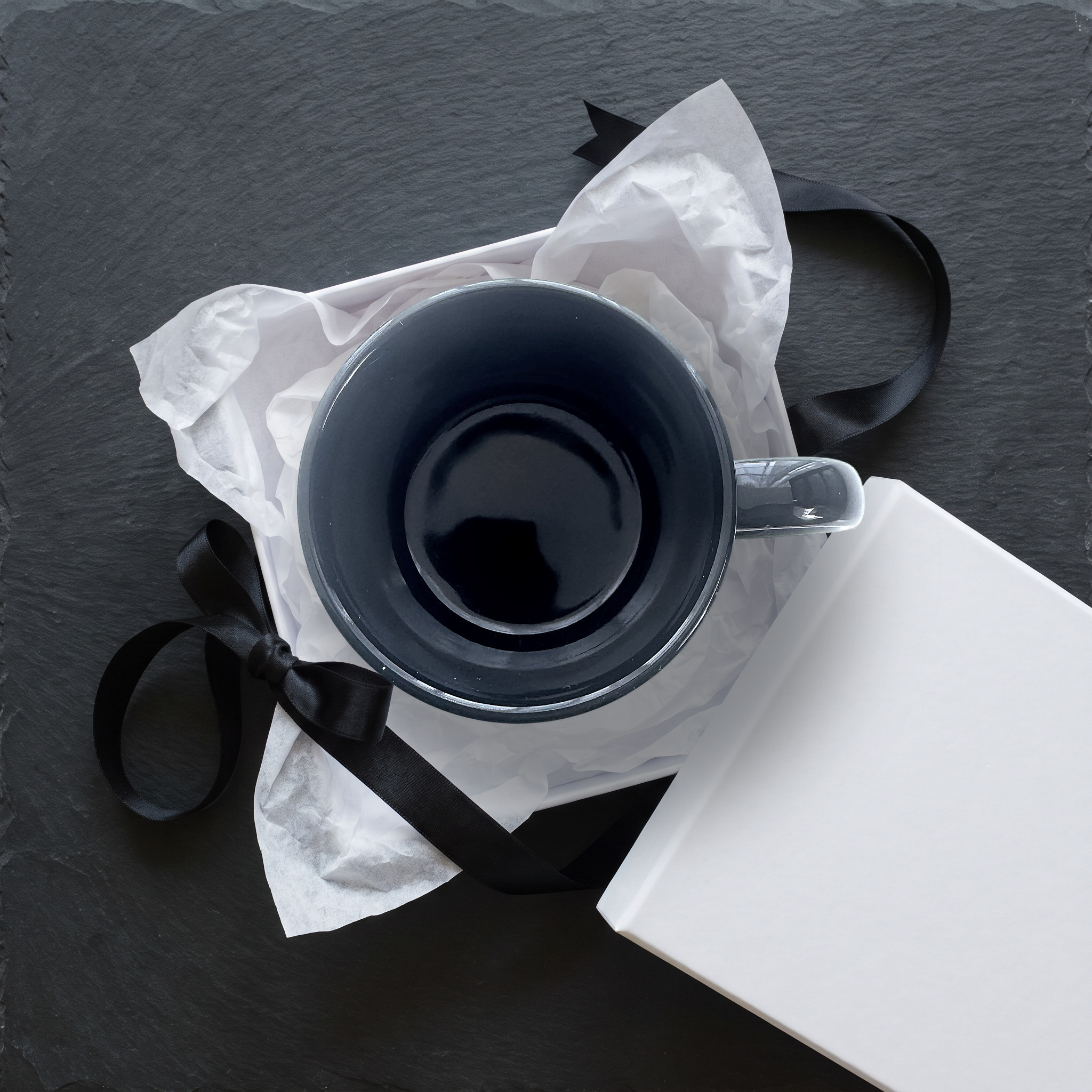 The mug nestled in a white gift box with tissue paper and a black ribbon
